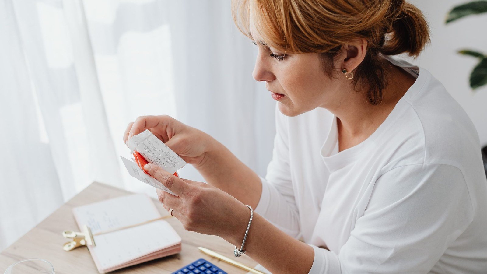 A woman at a desk reading through receipts with a notebook and calculator while working out a budget