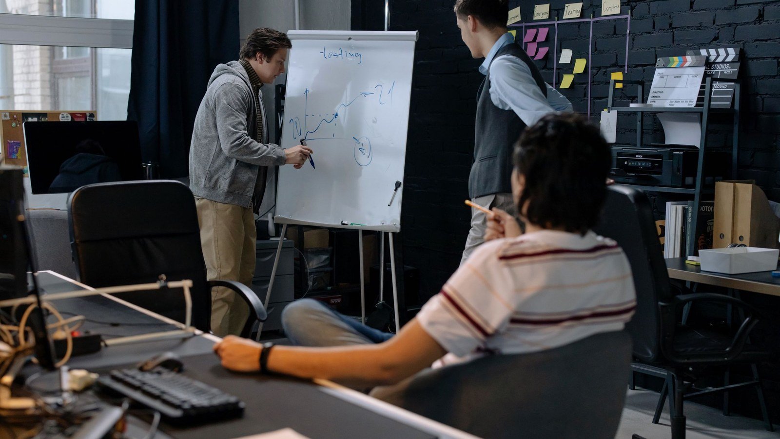 A small team in an office meeting while one colleague writes on a whiteboard and others take notes
