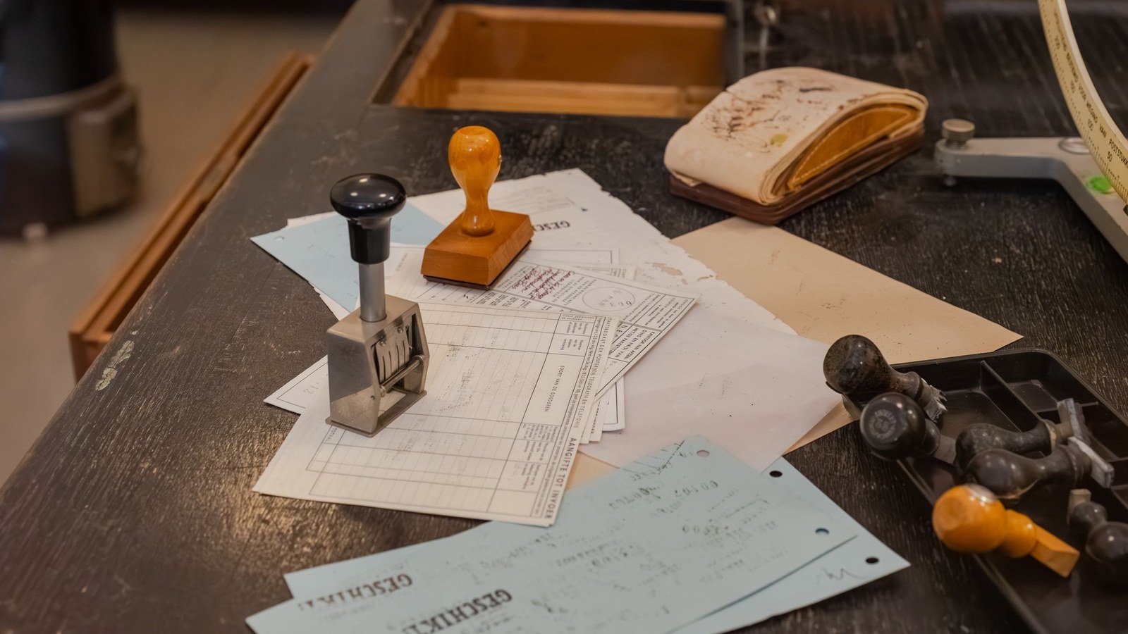 A cluttered office desk covered with paper forms, receipts and rubber stamps